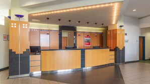 A modern reception desk with a wooden finish, a glass partition, and a digital screen.