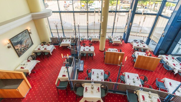 A restaurant with red carpet flooring, white tables, and chairs, large windows with a view of the street.