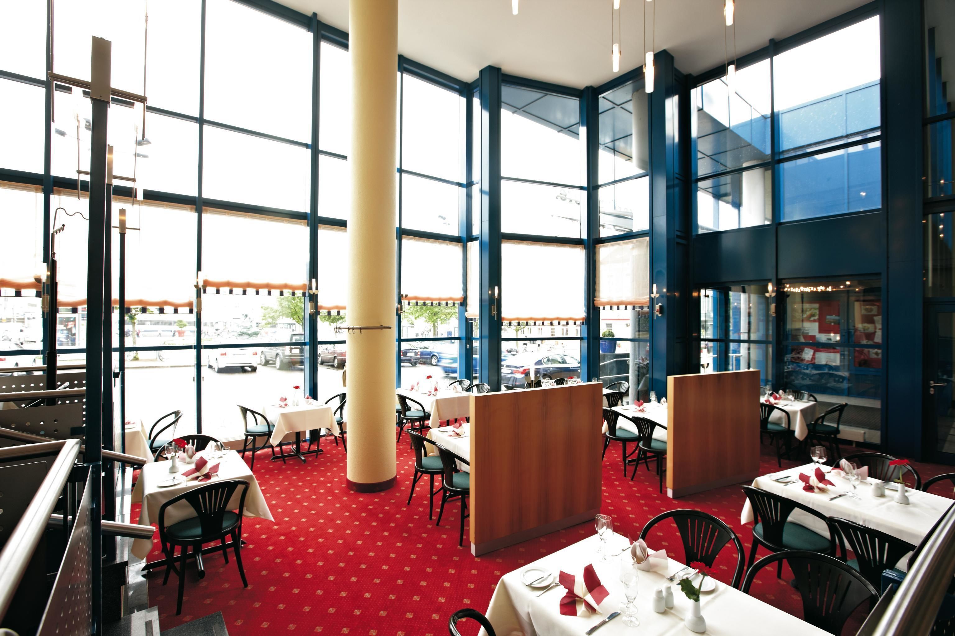 A restaurant with large windows, red carpet, and multiple dining tables.
