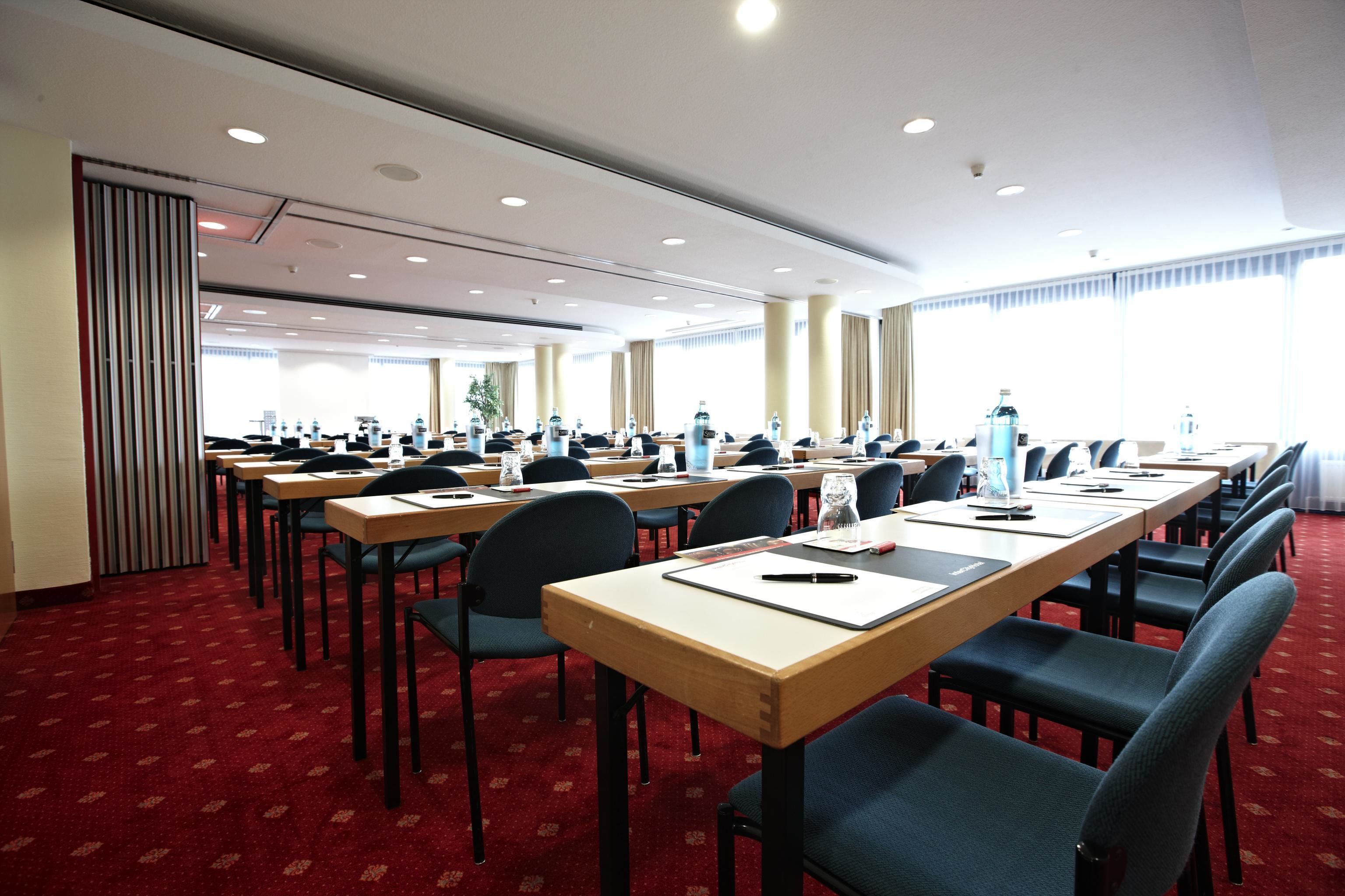 A conference room with long tables, chairs, and a red carpeted floor.