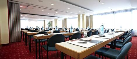Un salón de conferencias con mesas largas, sillas y piso cubierto de alfombra roja.