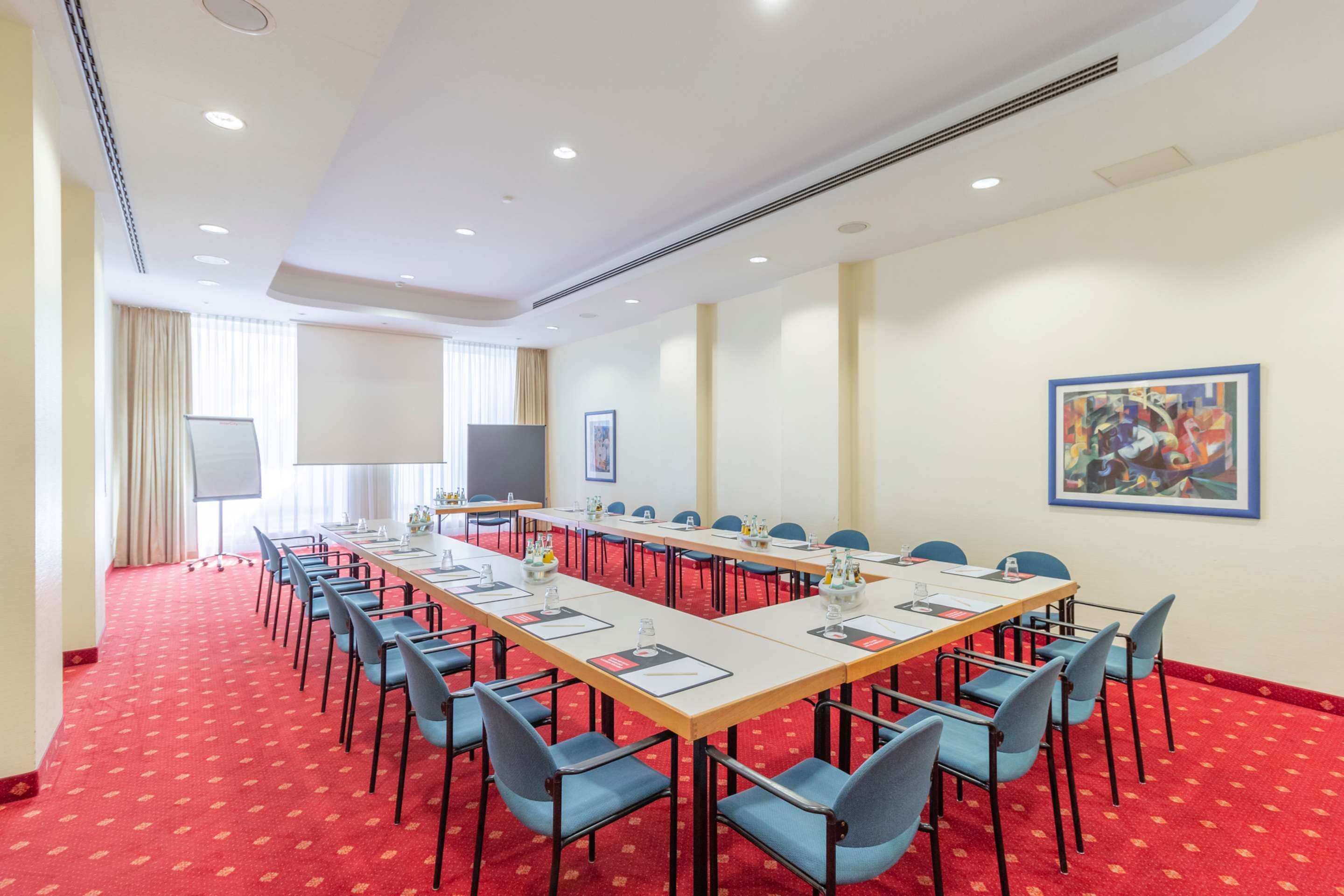 Un salón de conferencias con mesas largas y sillas, una pizarra y una pantalla de proyector.