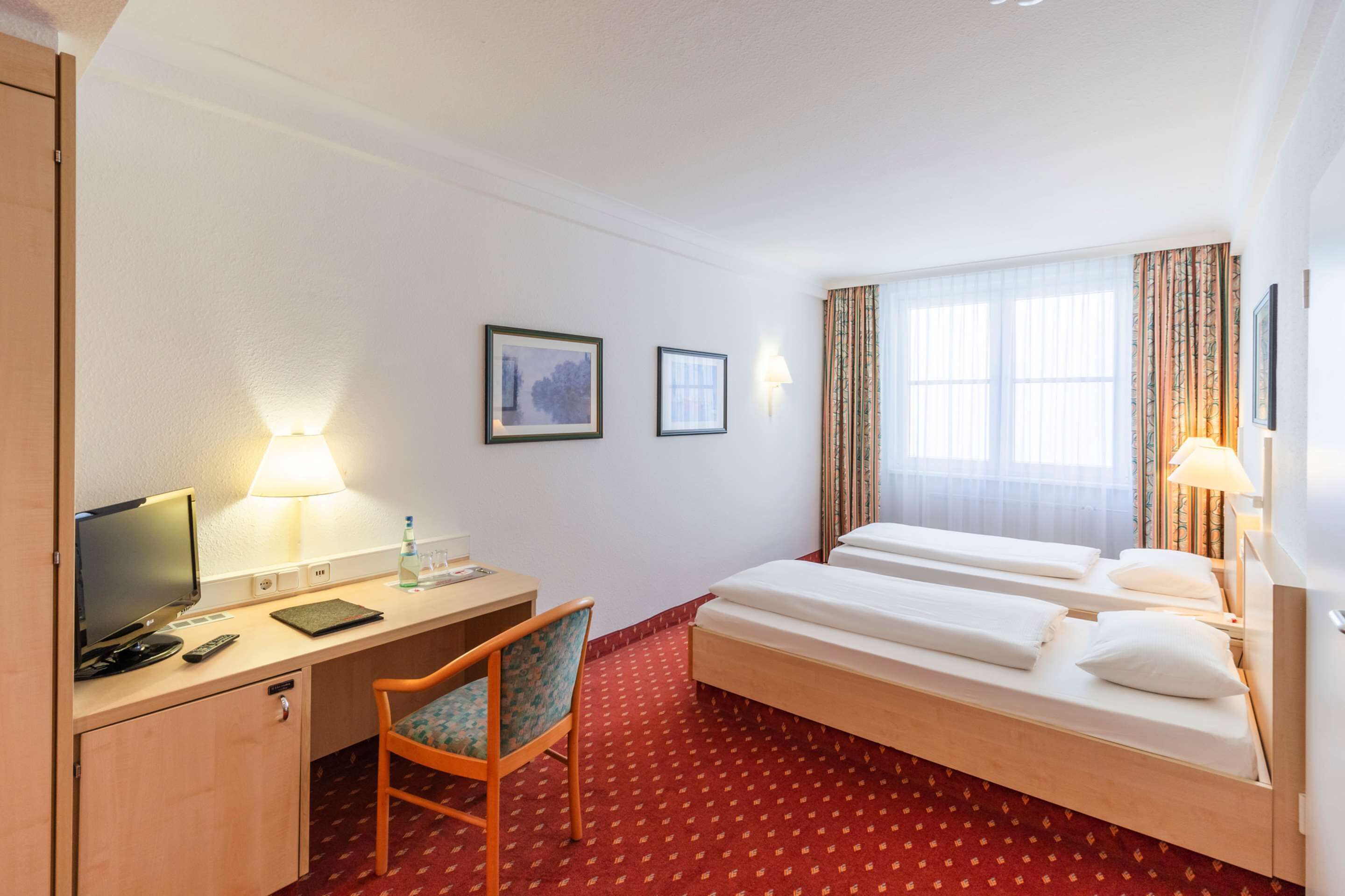 A hotel room with a desk, two beds, a chair, and a TV.