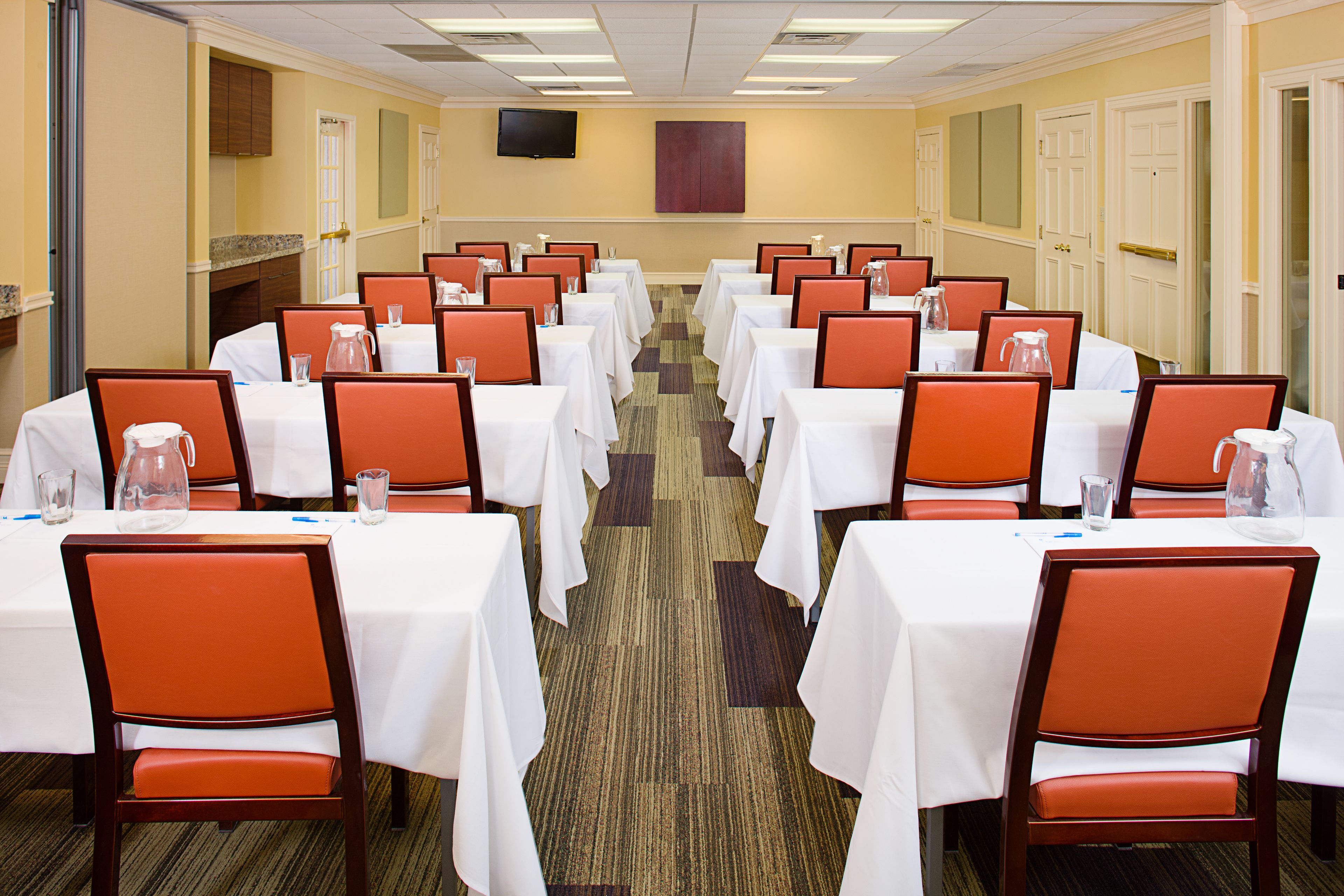 A conference room with rows of tables and chairs, equipped with water pitchers and glasses.