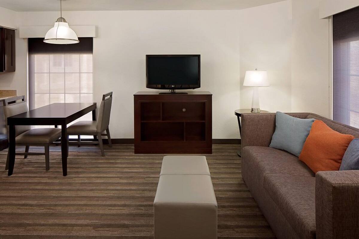 A hotel room with a dining table, a sofa, a TV, and a lamp.