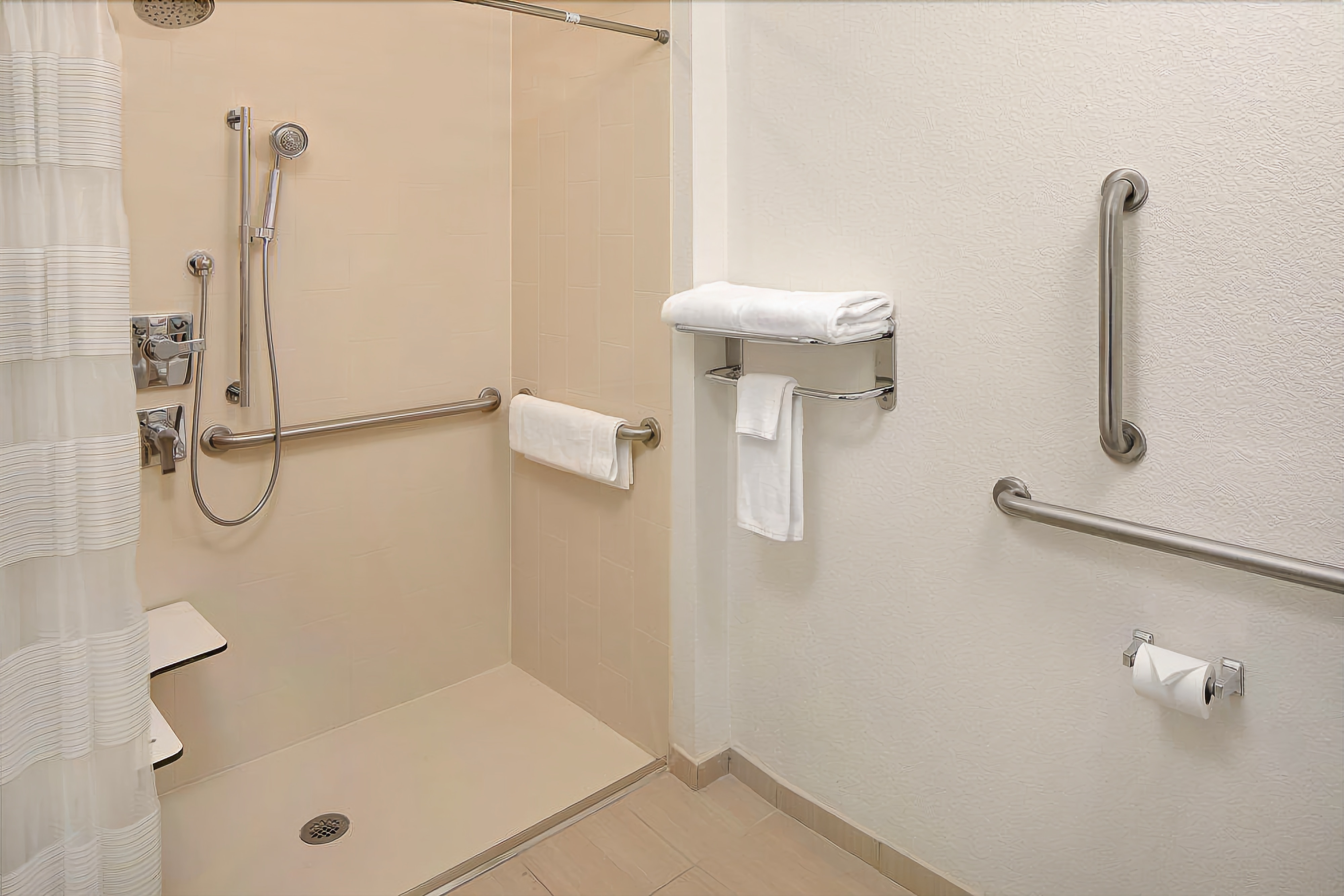 Une salle de bain équipée d’une douche à l’italienne, de barres d’appui, d’un porte-serviettes et d’un support à papier toilette.