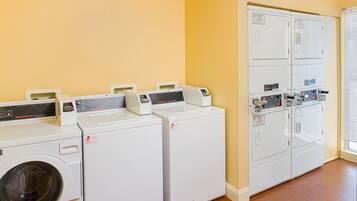 A laundry room with four front-loading washers and dryers, wooden floors, and a yellow wall.