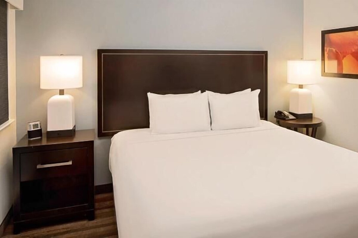 A neatly made bed with white linens, two bedside tables with lamps, and a framed picture on the wall.