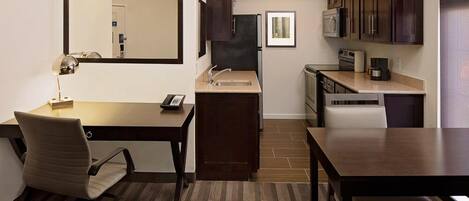 Habitación de hotel compacta con kitchenette, escritorio con silla, espejo grande y mesa de comedor.