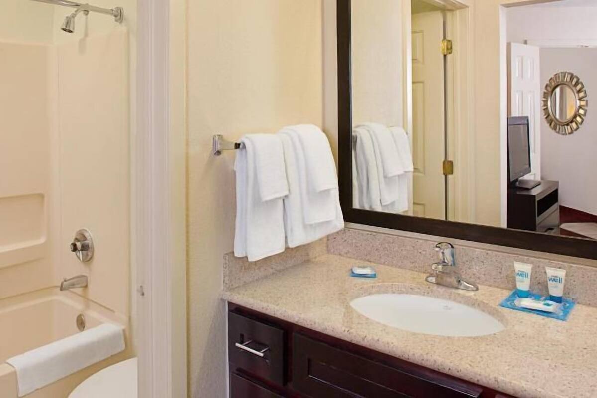 A bathroom with a bathtub, a sink, a mirror, and a towel rack.