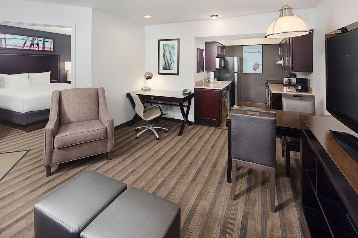 A hotel room with a bed, a desk, a chair, a television, and a kitchenette.