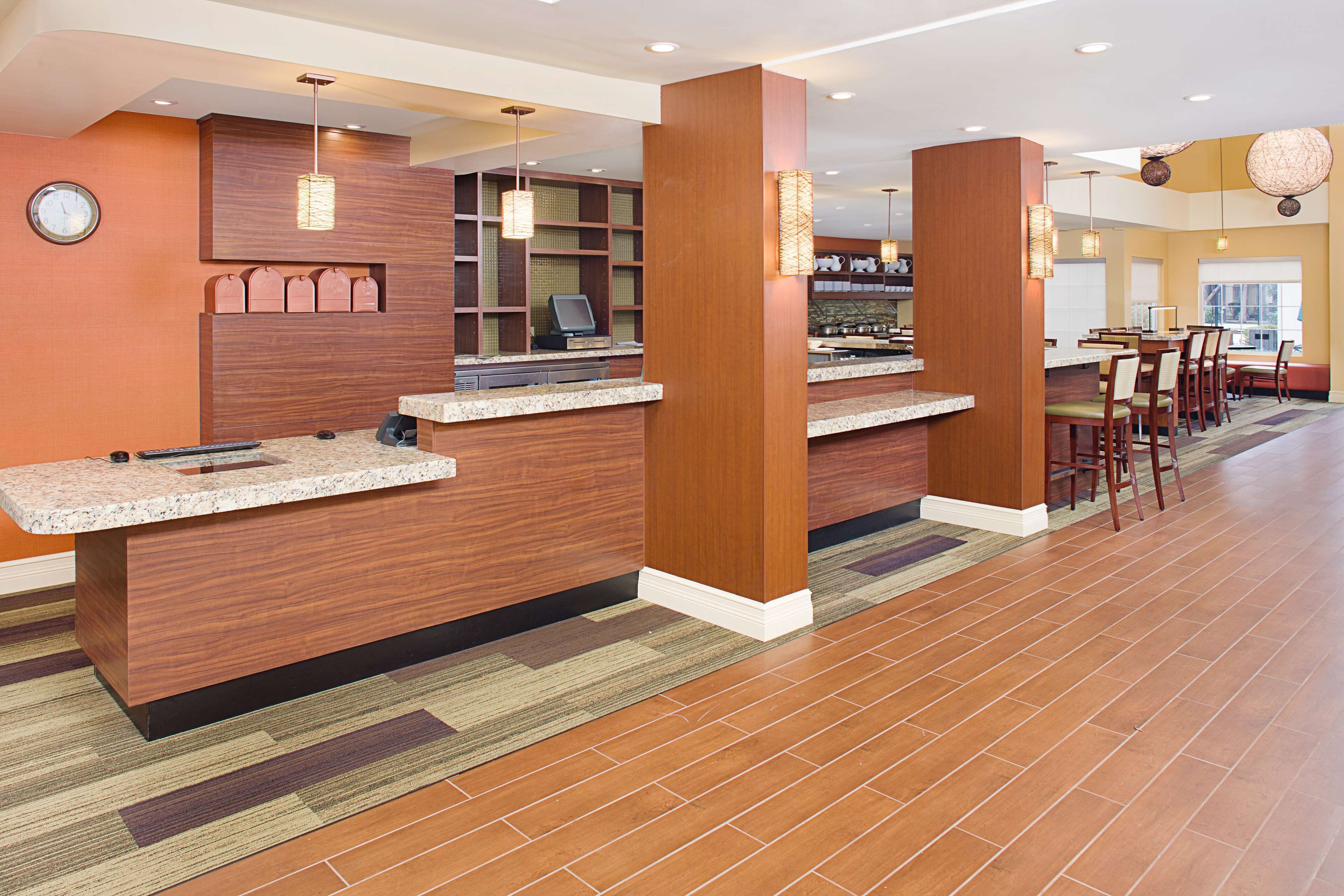 A hotel lobby with a reception desk, seating area, and a clock on the wall.