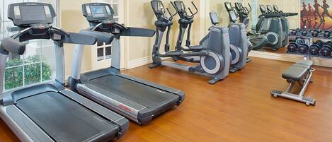 Un gimnasio con cintas de correr, elípticas y una banca.
