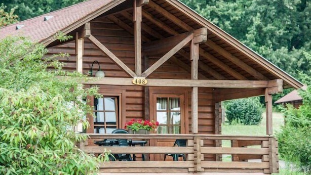 Uma cabana de madeira com varanda coberta, uma placa com o número 408 e uma mesa com cadeiras na parte externa.