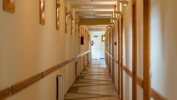 A long, narrow hotel corridor with doors on both sides, a tiled floor, and a ceiling with recessed lighting.