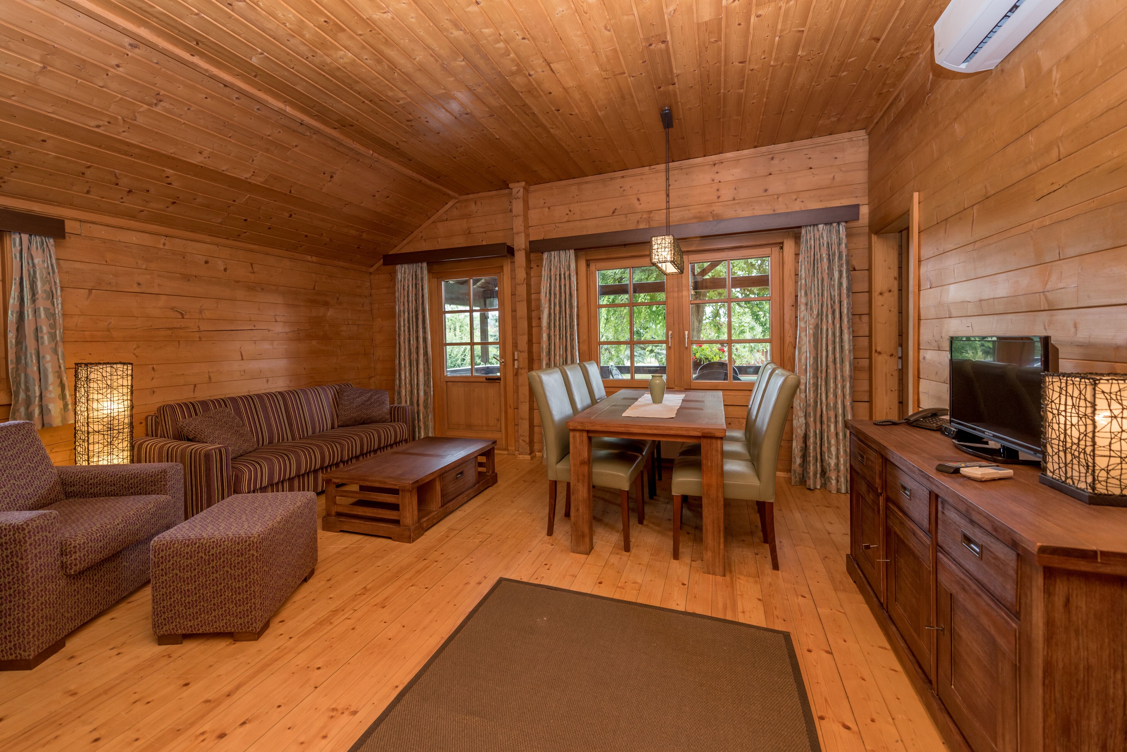 Ein Holzblockhaus-Interieur mit einer Couch, einem Esstisch, Stühlen und einem Fernseher.