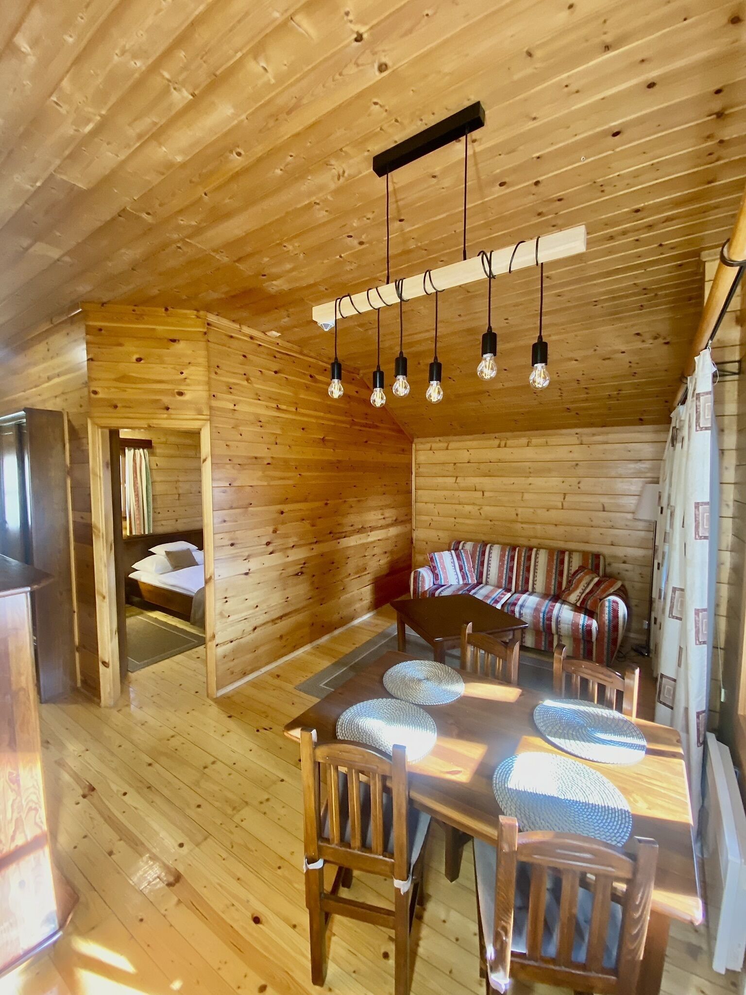 A wooden cabin interior with a dining area, a sofa, and a bed.