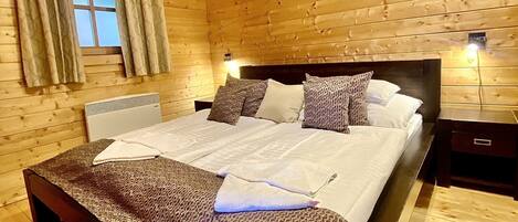 A wooden cabin bedroom with a bed, a window with curtains, a bedside table, and a nightstand.