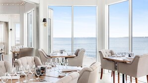 Un espace repas doté de grandes fenêtres donnant sur la mer, avec un intérieur moderne, des meubles aux couleurs claires et un design épuré et minimaliste.