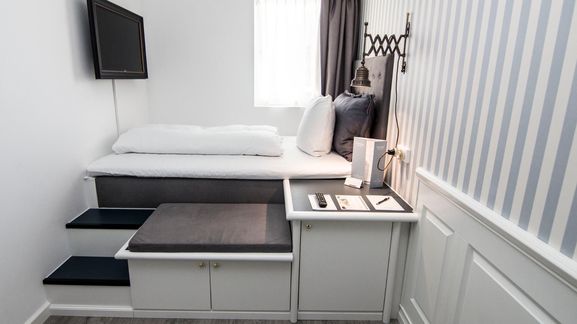 A compact room with a bed, a small desk, and a window with curtains.