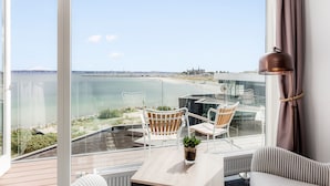 Un balcon avec vue sur la mer, deux chaises blanches, une petite table et une plante en pot.