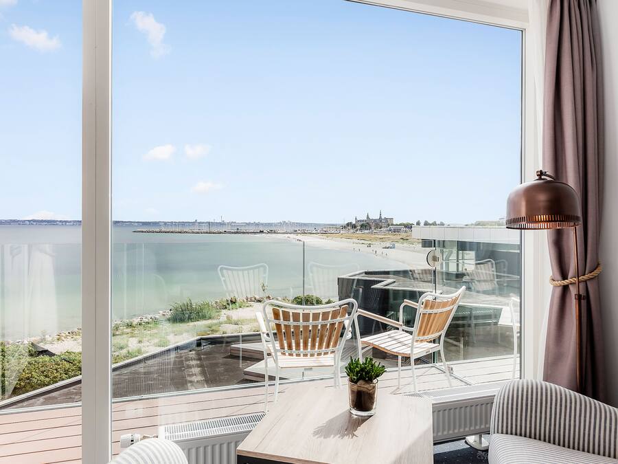 A balcony with a view of the sea, two white chairs, a small table, and a potted plant.