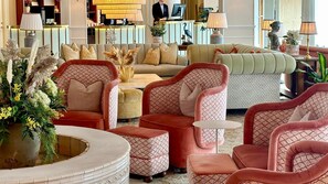 A spacious lobby with multiple seating areas, including sofas and armchairs, a reception desk, and a decorative plant arrangement.