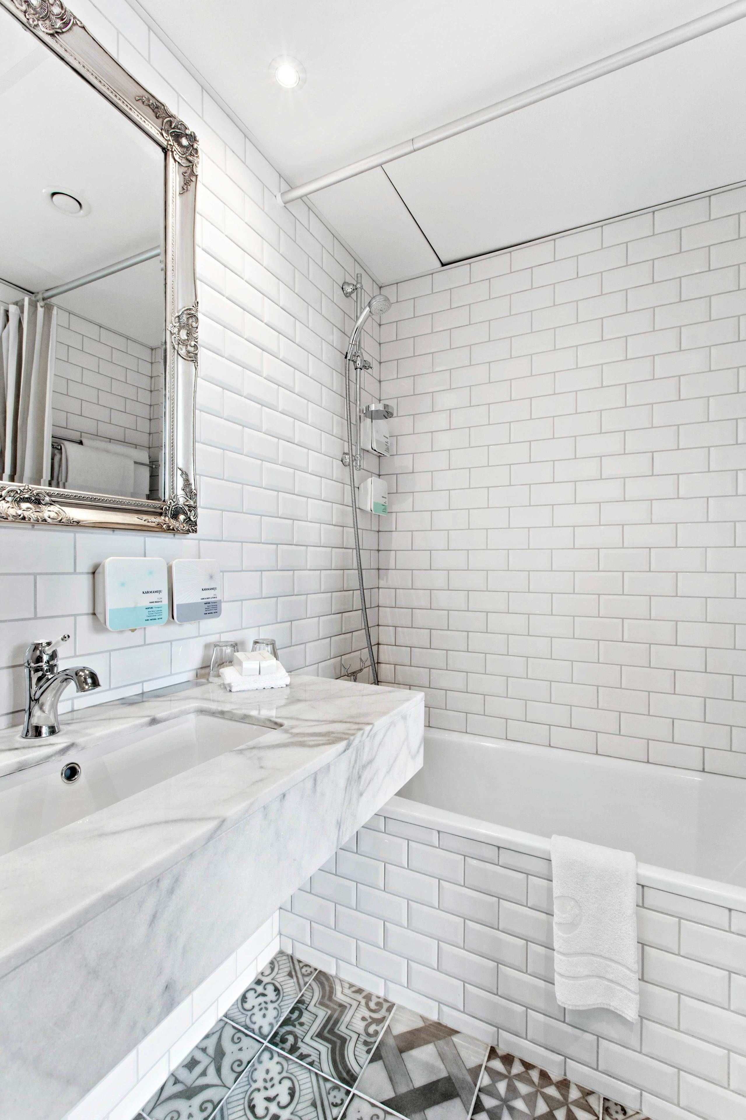 A bathroom with white subway tiles, a large ornate mirror, a marble sink, a bathtub, and patterned floor tiles.