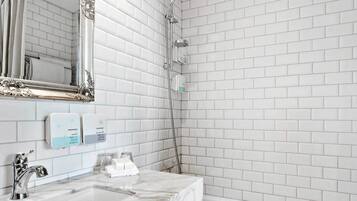 A bathroom with white subway tiles, a large ornate mirror, a marble sink, a bathtub, and patterned floor tiles.