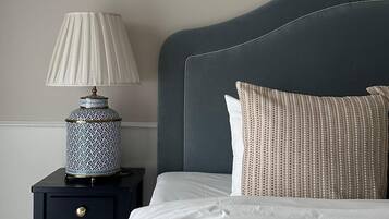 A neatly made bed with a dark headboard, a white pillow, and a patterned pillow. There is a small bedside table with a lamp and a decorative vase.