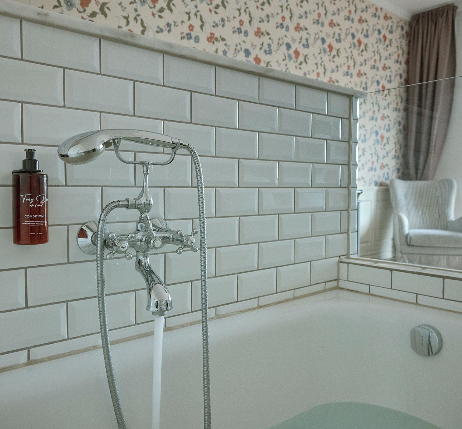 Un baño con ducha, un frasco de acondicionador y una silla.