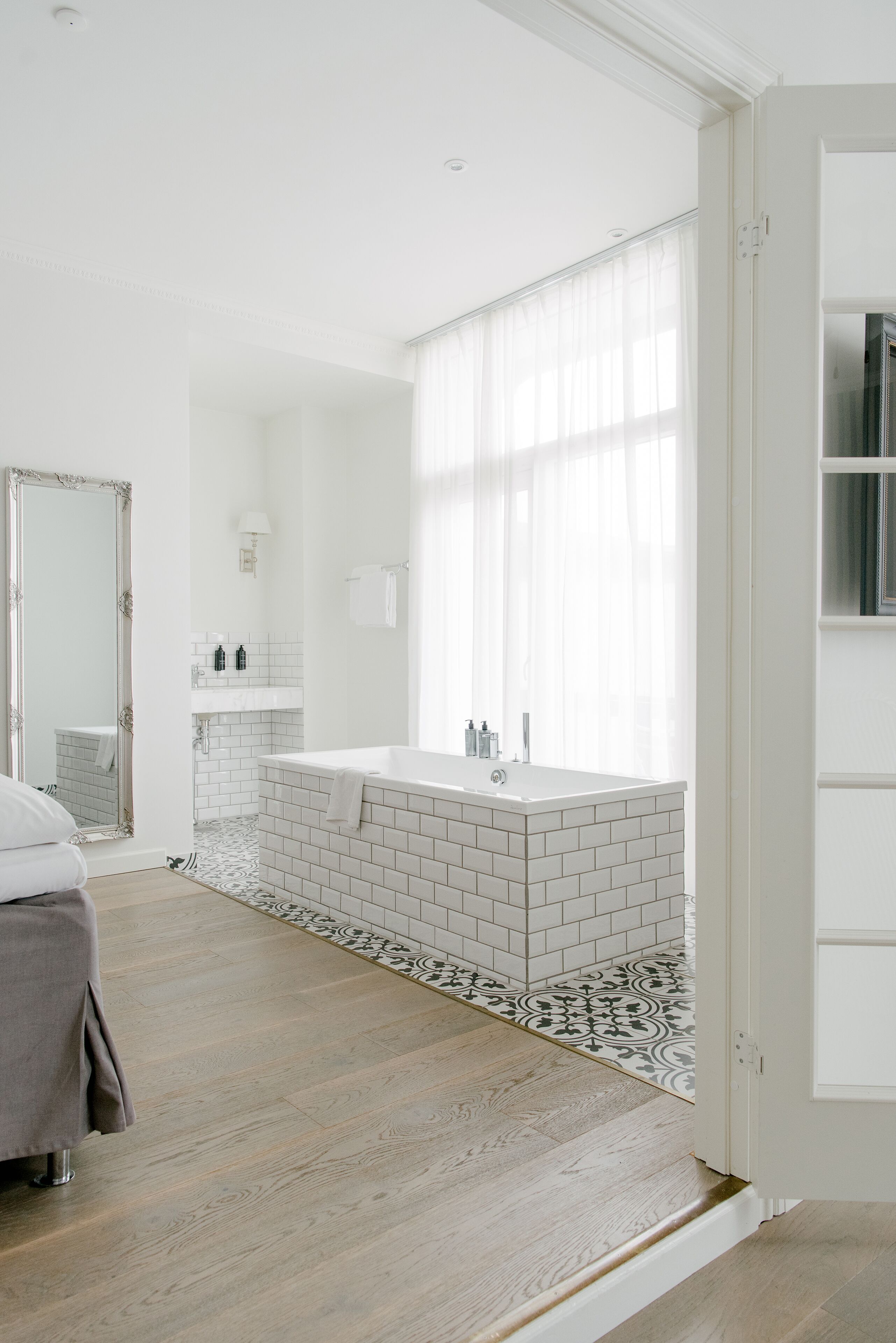 A modern bathroom with a large bathtub, white tiles, and a mirror.