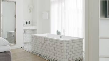 A modern bathroom with a large bathtub, white tiles, and a mirror.