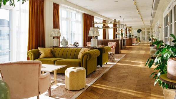 A spacious hotel lobby with a green sofa, a pink armchair, and a wooden reception desk.