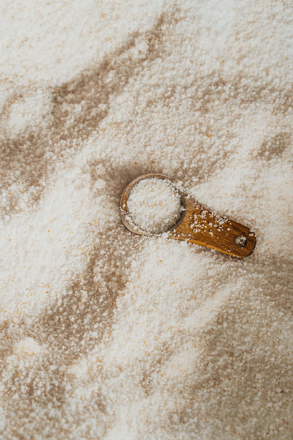 Una cuchara de madera con una cucharada de polvo blanco, presumiblemente sal, sobre una superficie rugosa.