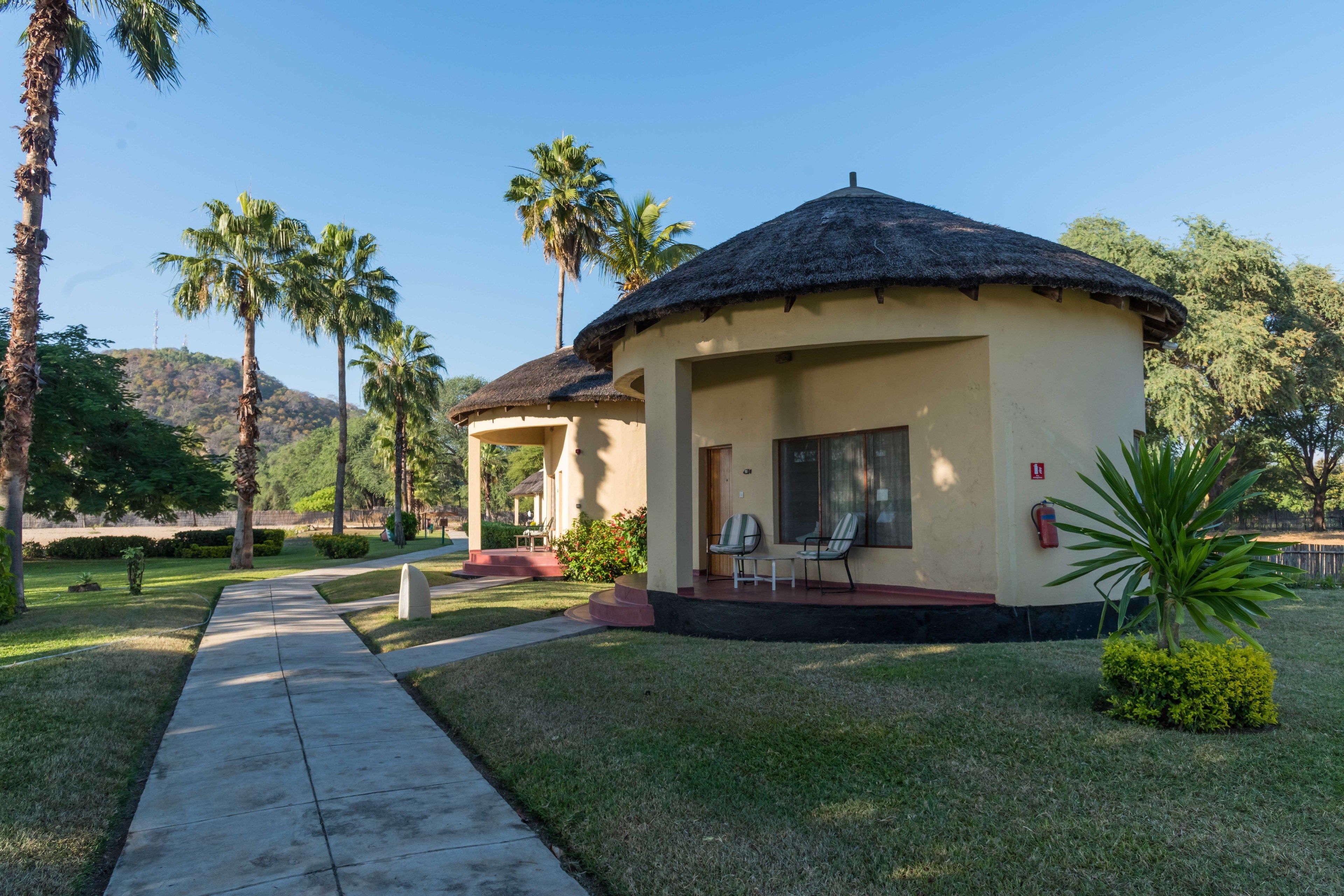 A small, single-story building with a thatched roof, surrounded by palm trees and a clear sky.