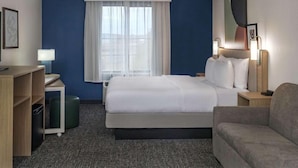 Habitación de hotel con cama, escritorio, silla, lámpara y ventana con cortinas.
