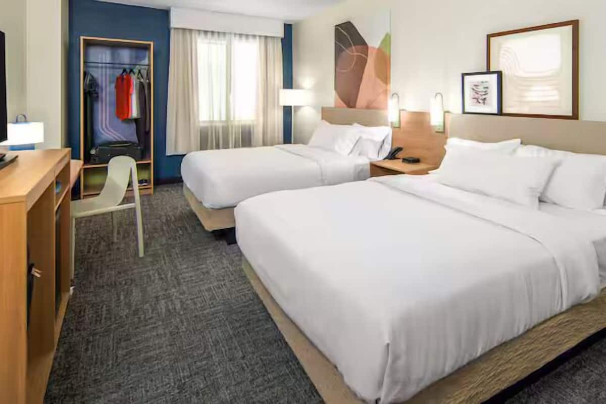 Habitación de hotel con dos camas, un escritorio, una silla, un armario y una ventana con cortinas.