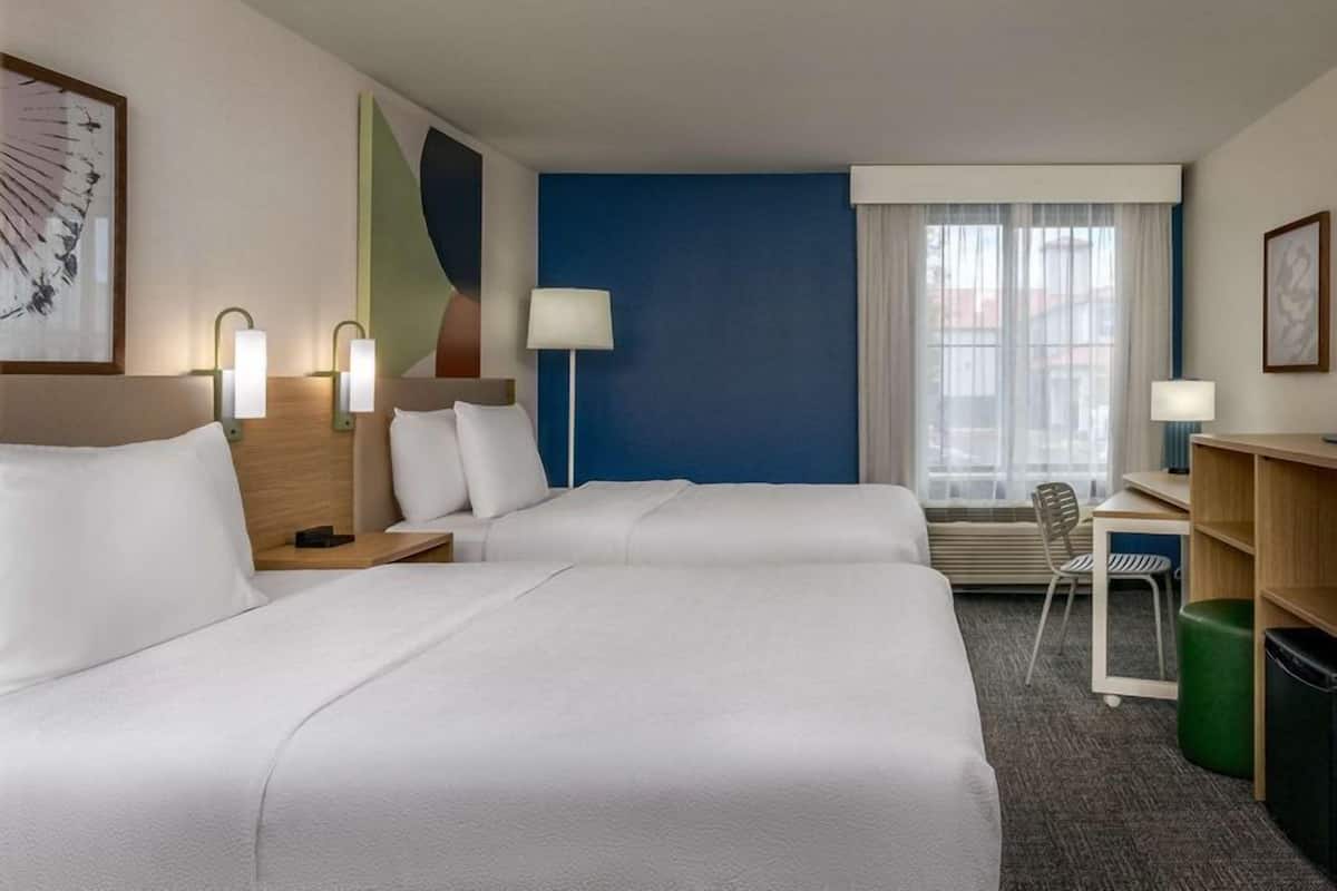 Habitación de hotel con dos camas, un escritorio, una silla y una ventana con cortinas.