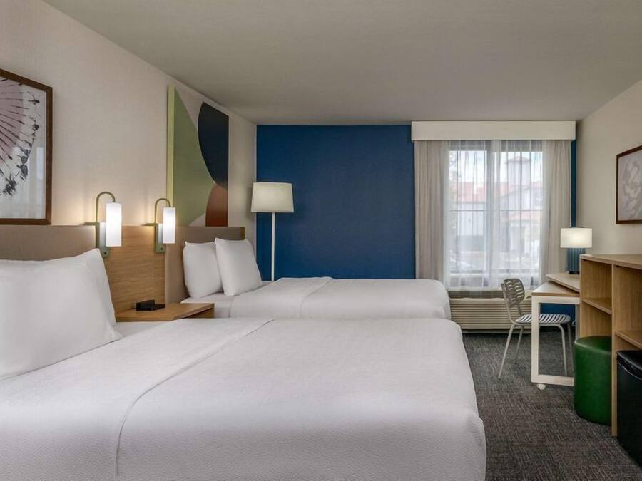 Habitación de hotel con dos camas, un escritorio, una silla y una ventana con cortinas.