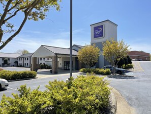 A Sleep Inn by Choice Hotels with a parking lot, a covered entrance, and surrounding greenery.