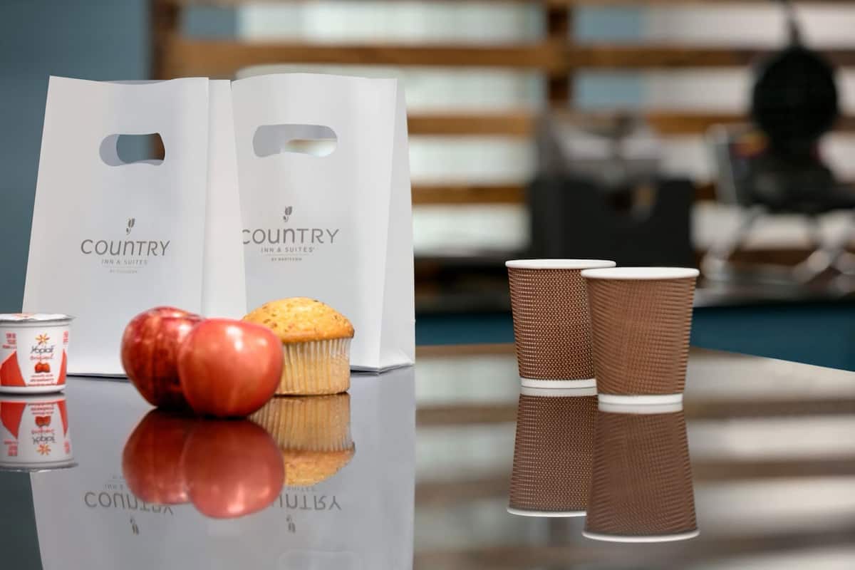 Una mesa con un muffin, una manzana, una lata y dos vasos de papel.