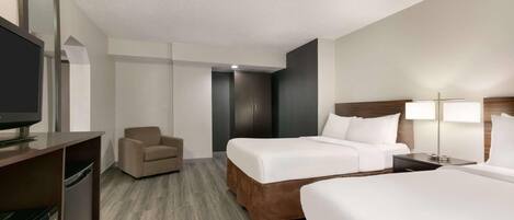 A hotel room with a bed, a chair, a desk with a television, and a lamp.