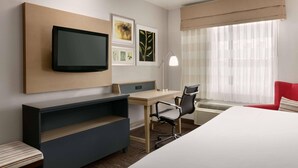 A hotel room with a bed, a desk, a chair, a TV, and artwork on the wall.