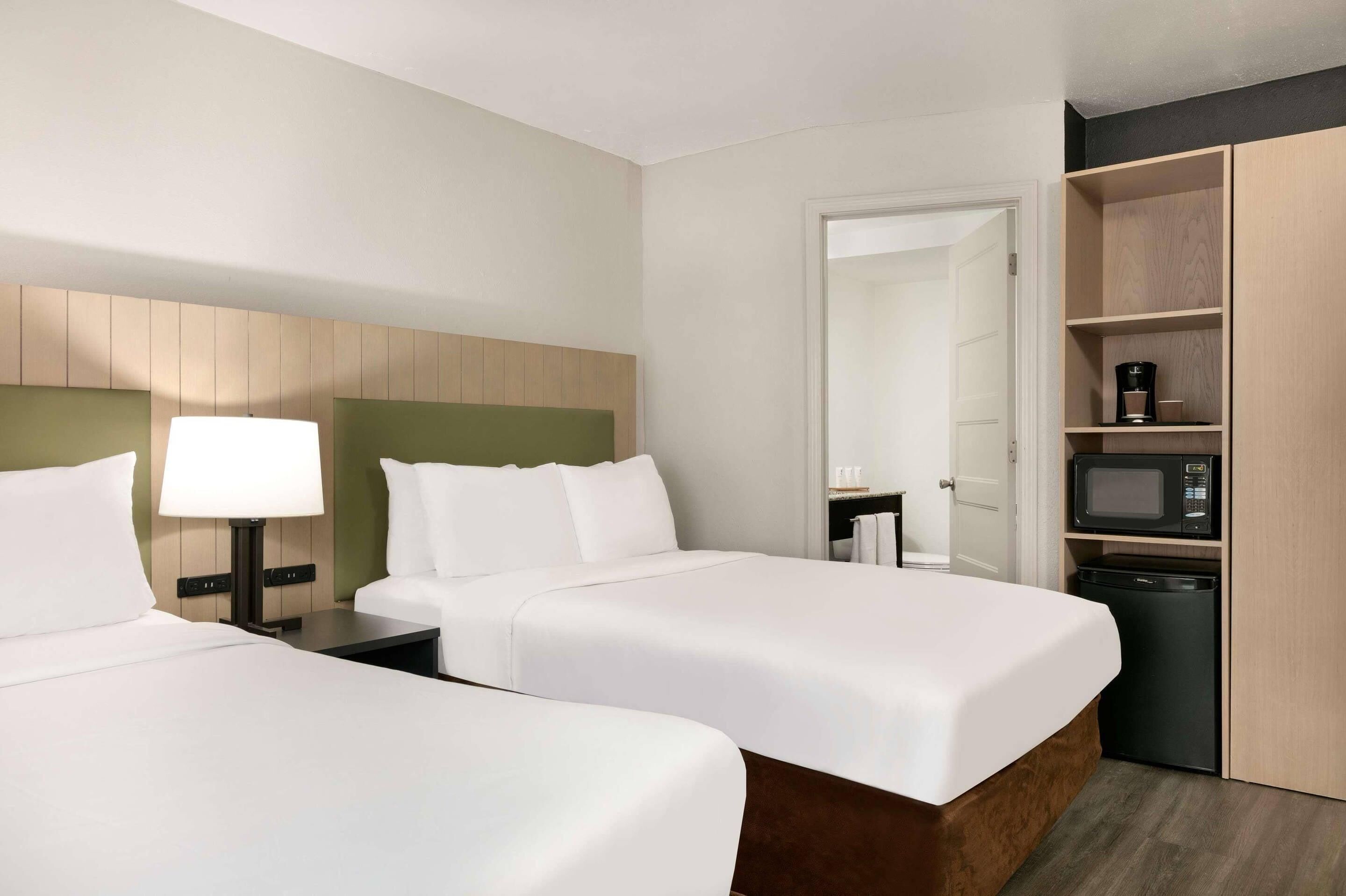 Habitación de hotel con dos camas, una mesita de noche con lámpara, microondas y refrigerador pequeño.