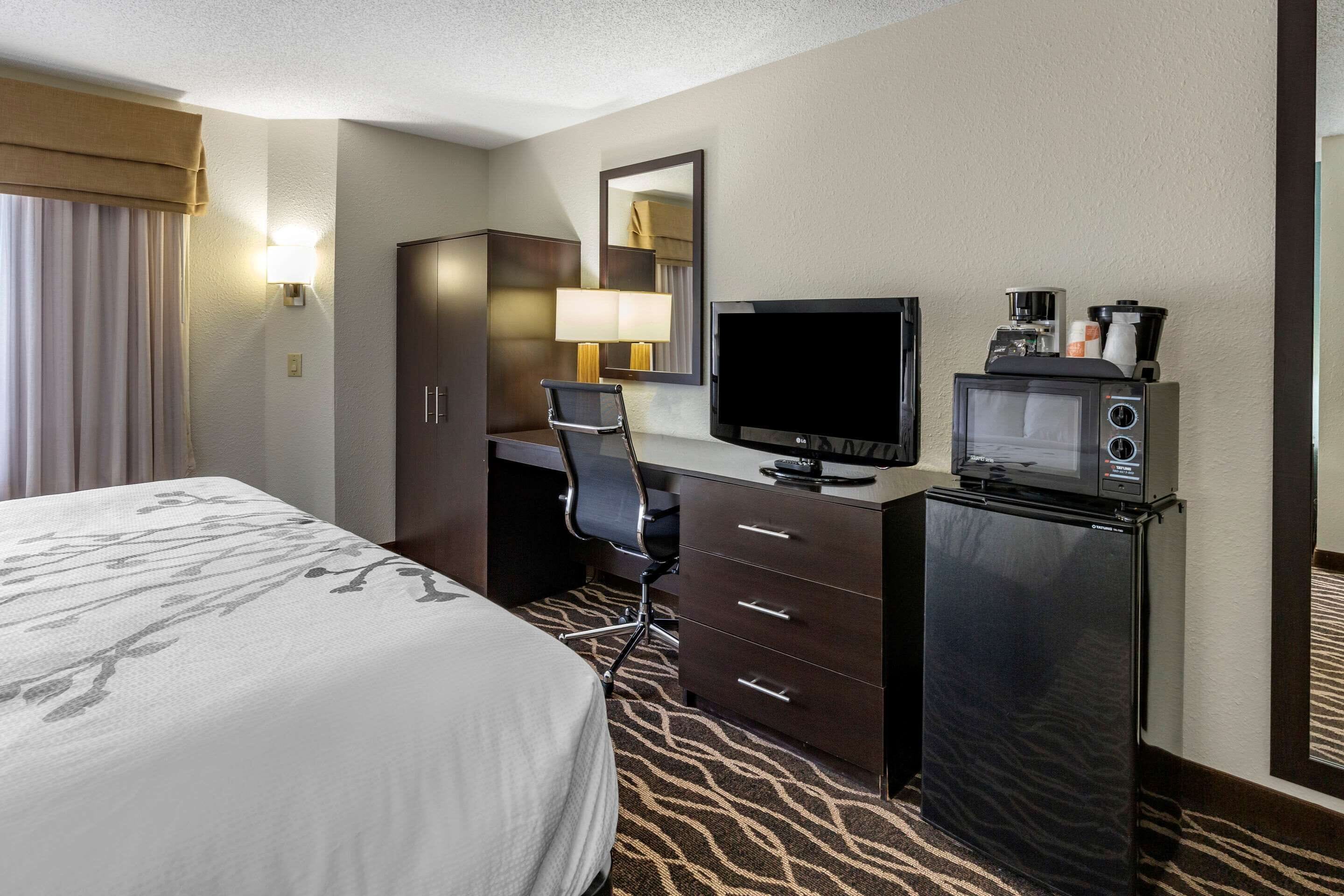 A hotel room with a bed, a desk with a computer, a television, a microwave, and a coffee maker.
