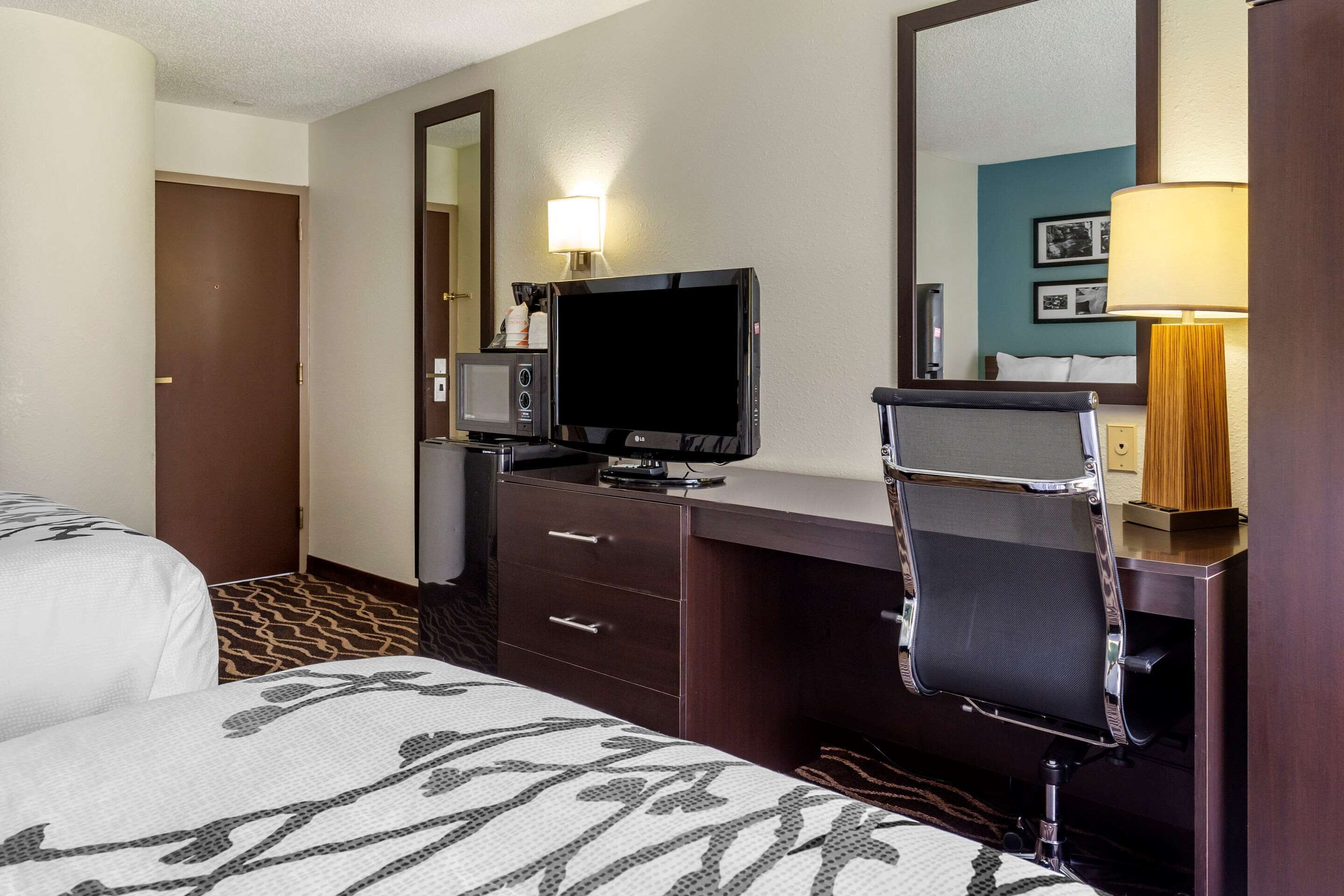 A hotel room with a bed, a desk with a television, a mirror, and a lamp.