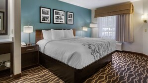 A hotel room with a bed, nightstands, a desk, and a window with curtains. - Sleep Inn Fayetteville I-95 (Fayetteville)