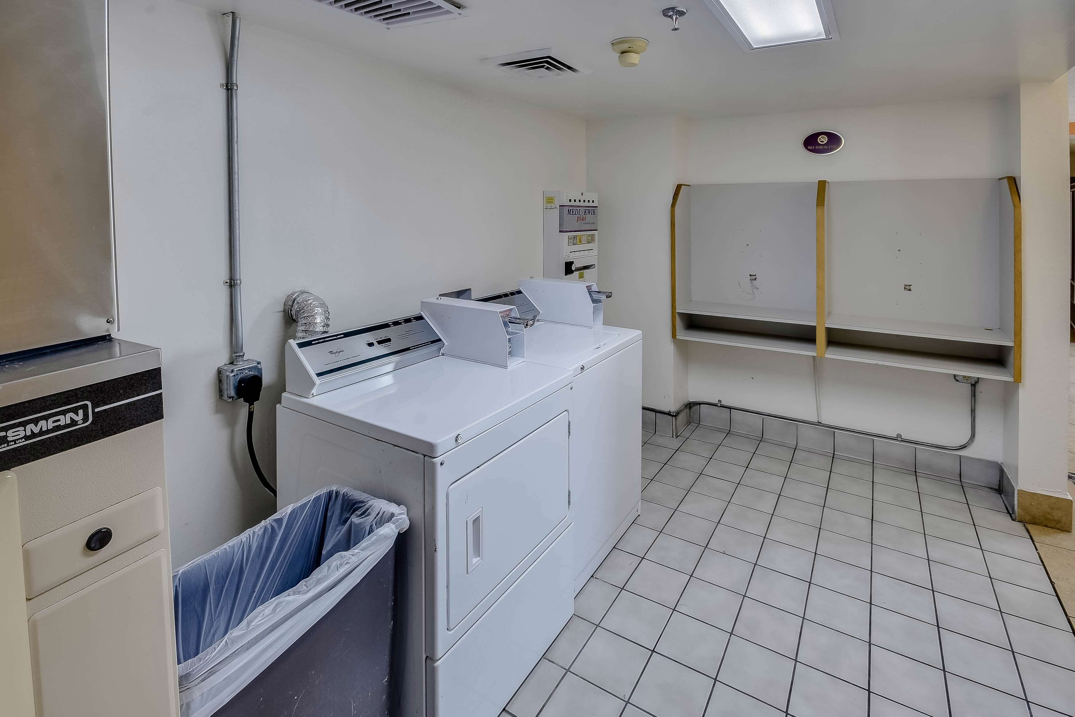 A laundry room with a washing machine, a dryer, and a trash bin.