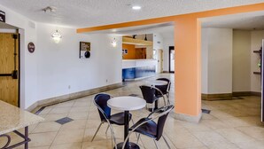 A hotel lobby with a reception desk, a dining area with tables and chairs, and a kitchen in the background. - Motel 6 Katy, TX - Houston (Katy)